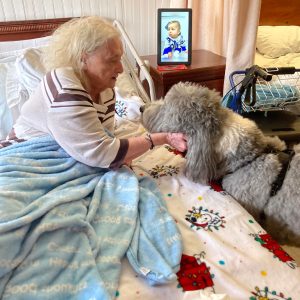 Woman in a nursing home laying in bed petting a therapy dog.
